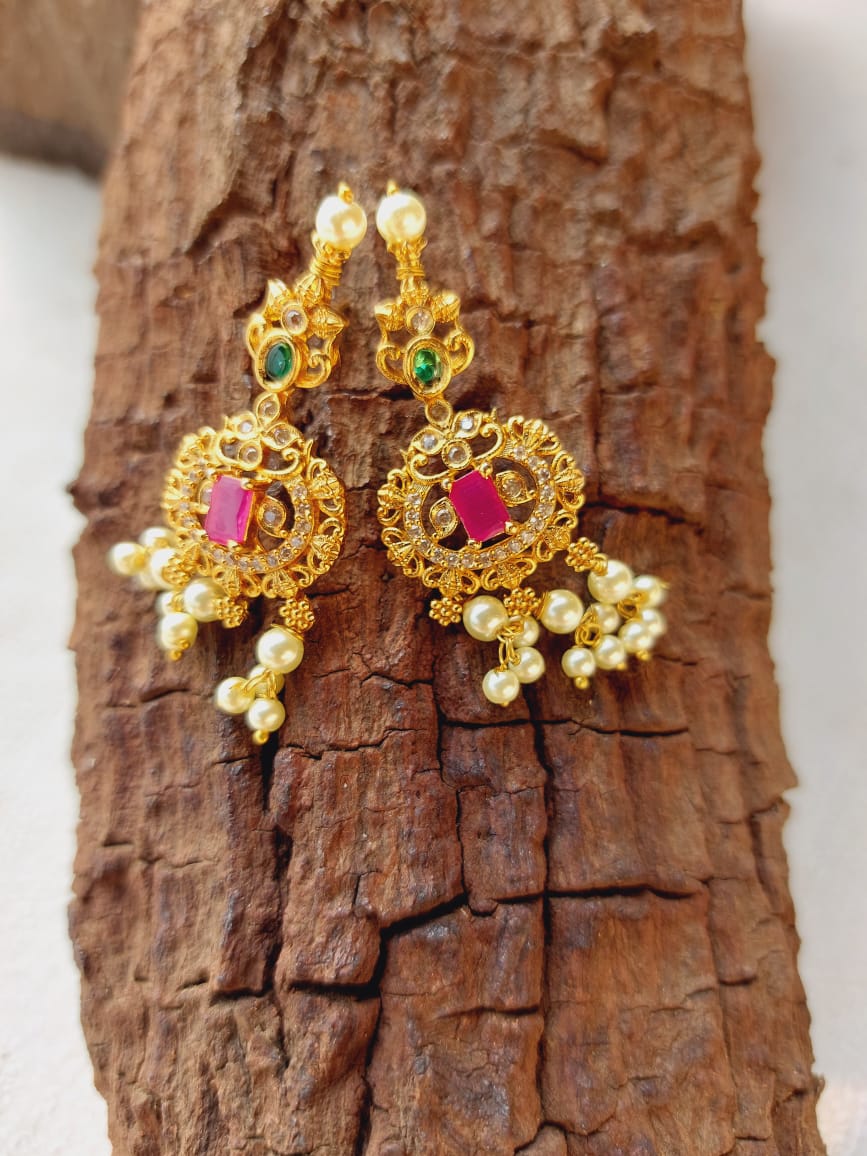 Exquisite Gold and Precious Stone Dangler Earrings
Intricate gold filigree design adorned with vibrant ruby and emerald stones, delicately accented by lustrous pearls, showcased on a rustic wooden surface.