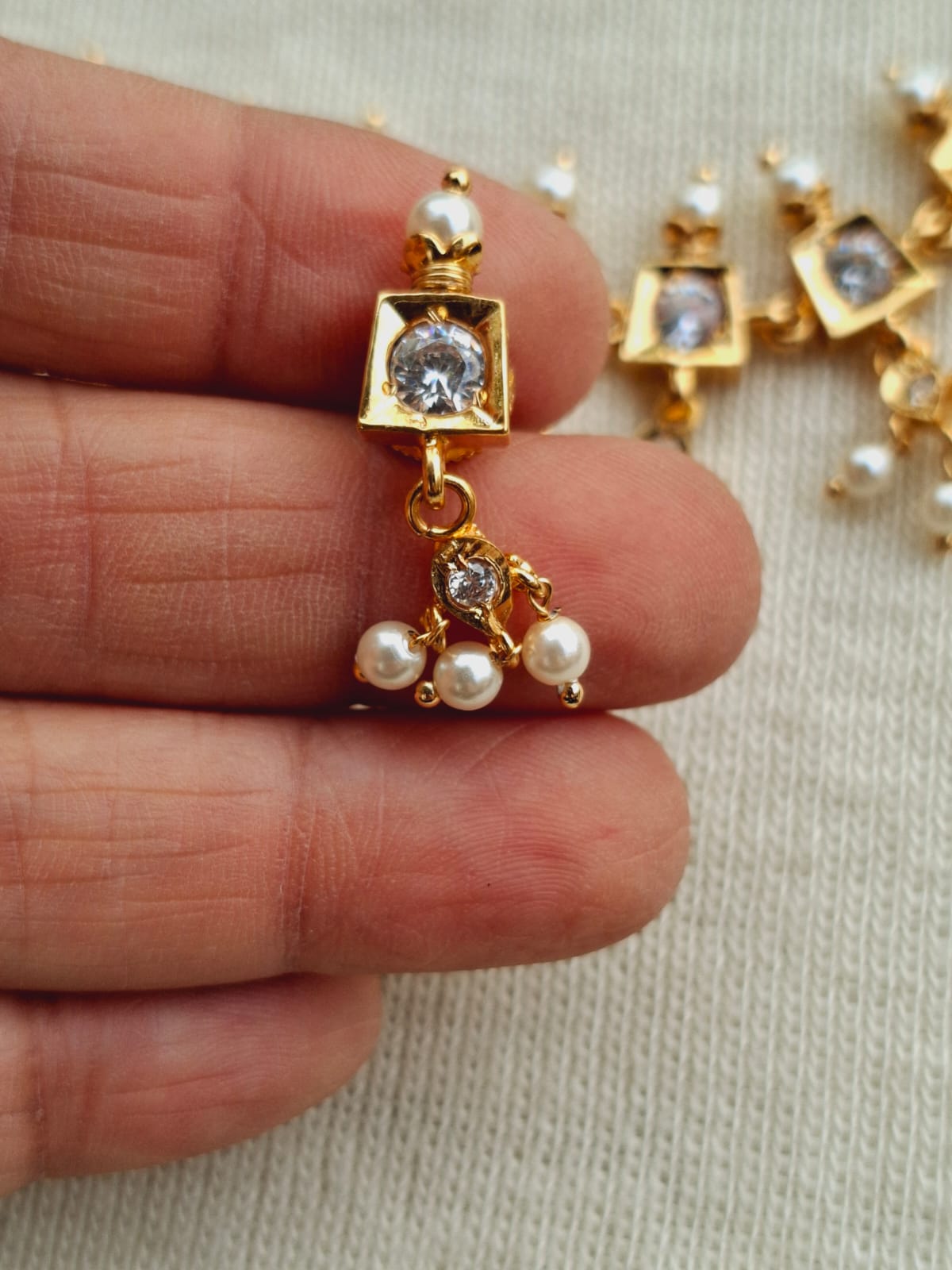 Beautiful white traditional designer jewelry set with square pendant adorned with crystal stones and pearl drops, showcased in a hand-held image.