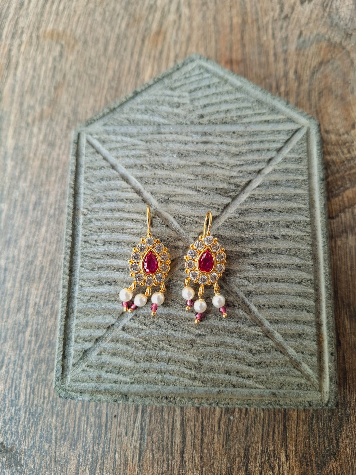 Detailed red gemstone earrings displayed on wooden background with textured grain pattern