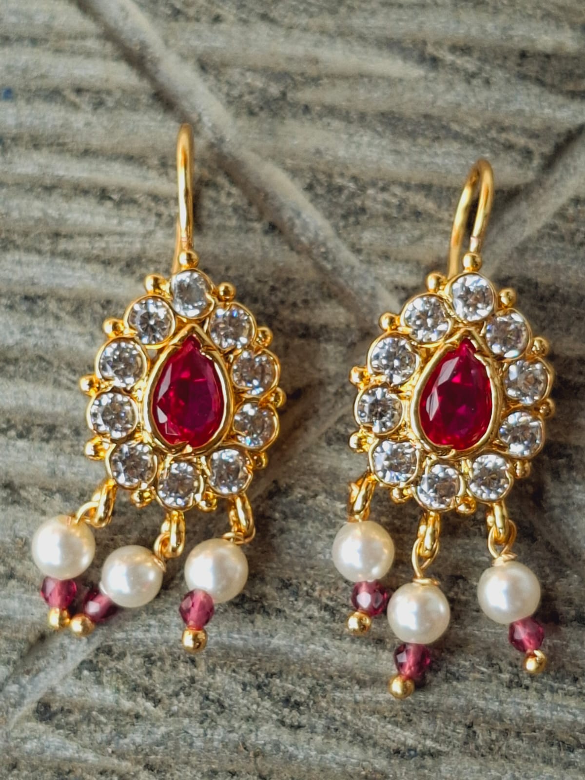 Elegant gold-toned Designer Badam Bugdi earrings featuring red and clear gemstones with dangling pearl accents, displayed against a neutral background.