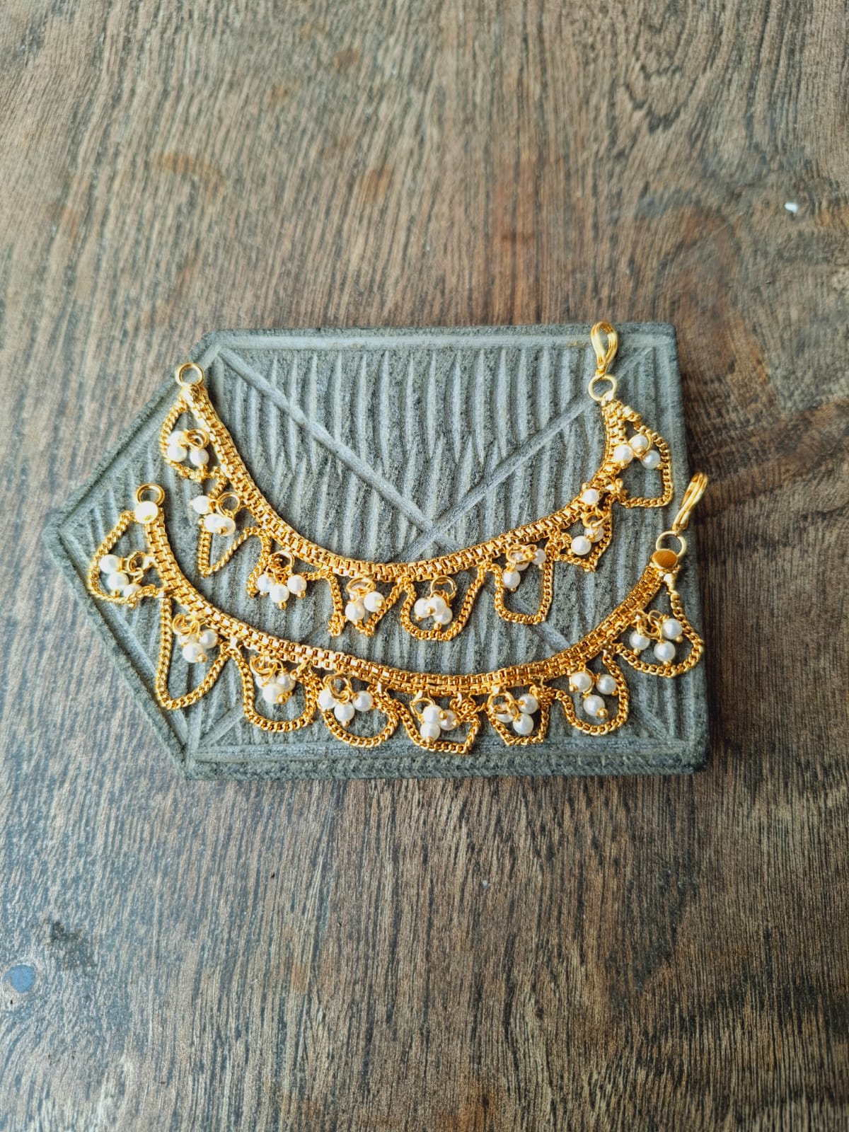 Elegant Golden Pearl Ear Chain - Intricate pearl-studded golden accessory displayed on a rustic wooden surface.