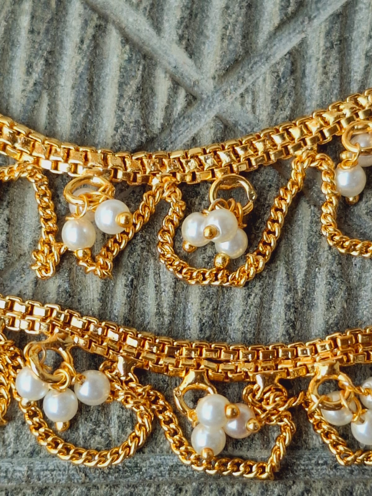 Ornate golden chain with pearl accents. The image shows a designer golden chain ear chain with intricate dangles featuring pearl embellishments against a textured grey background.