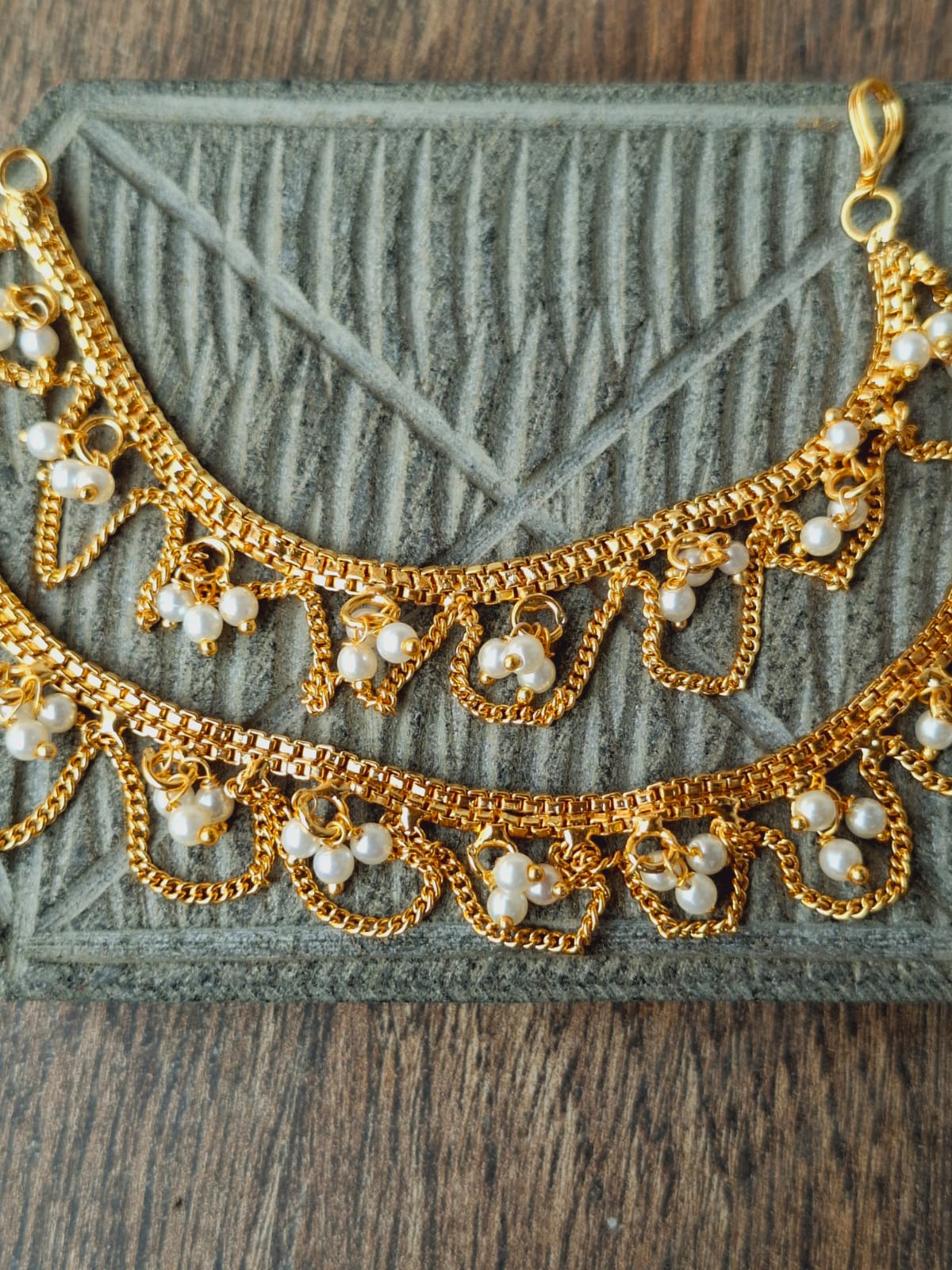 Ornate golden ear chains with intricate pearl accents displayed on a textured gray background.