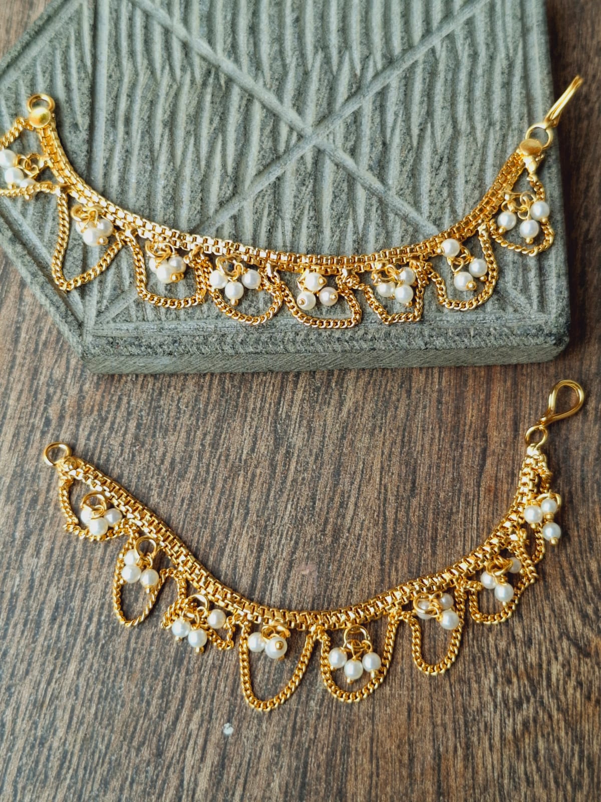 Elegant golden designer pearl ear chain with intricate beaded and chain detailing, displayed on a textured green fabric background.