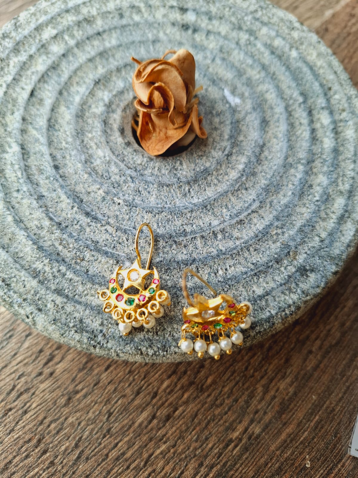 Ornate gold-toned chandelier earrings with multicolored gemstones displayed on a textured grey mat.