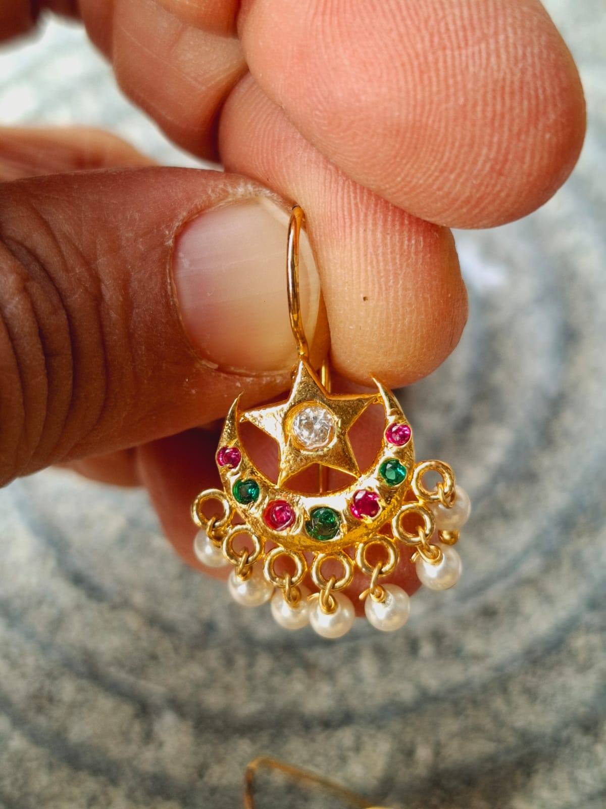 Multicolored star-shaped Chandrakor Bugdi earrings with dangling gems in a gold metal frame, held close in hand