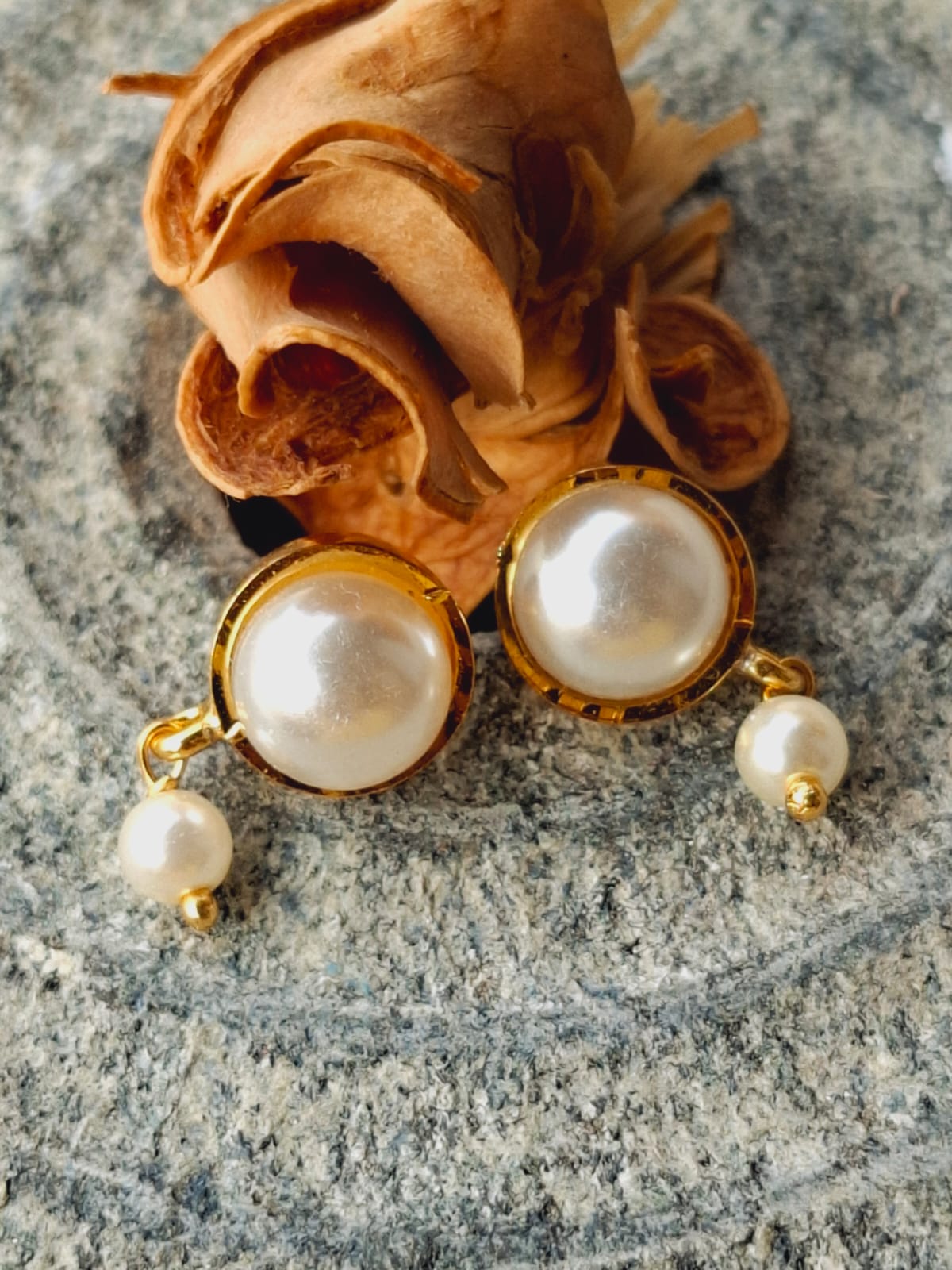 Elegant pearl earrings with gold accents displayed on a floral cloth background.