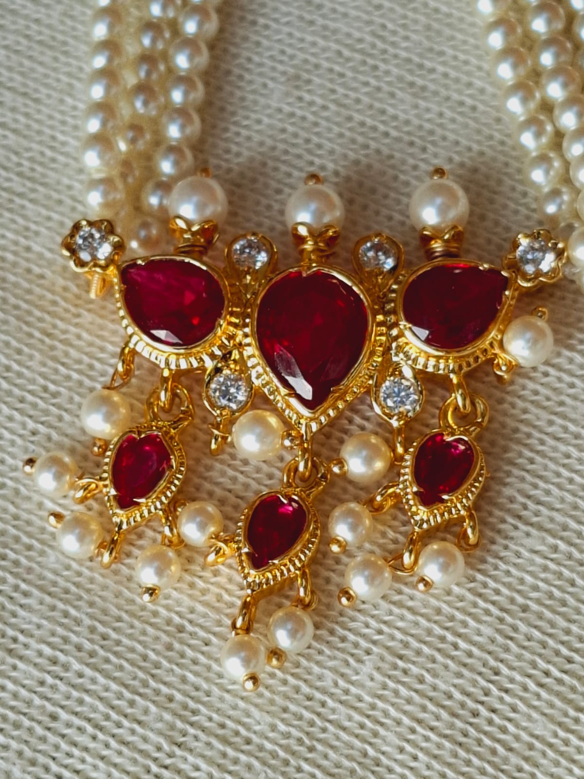 Elegant golden pendant with ruby gemstones and white pearls, displayed against a light background.