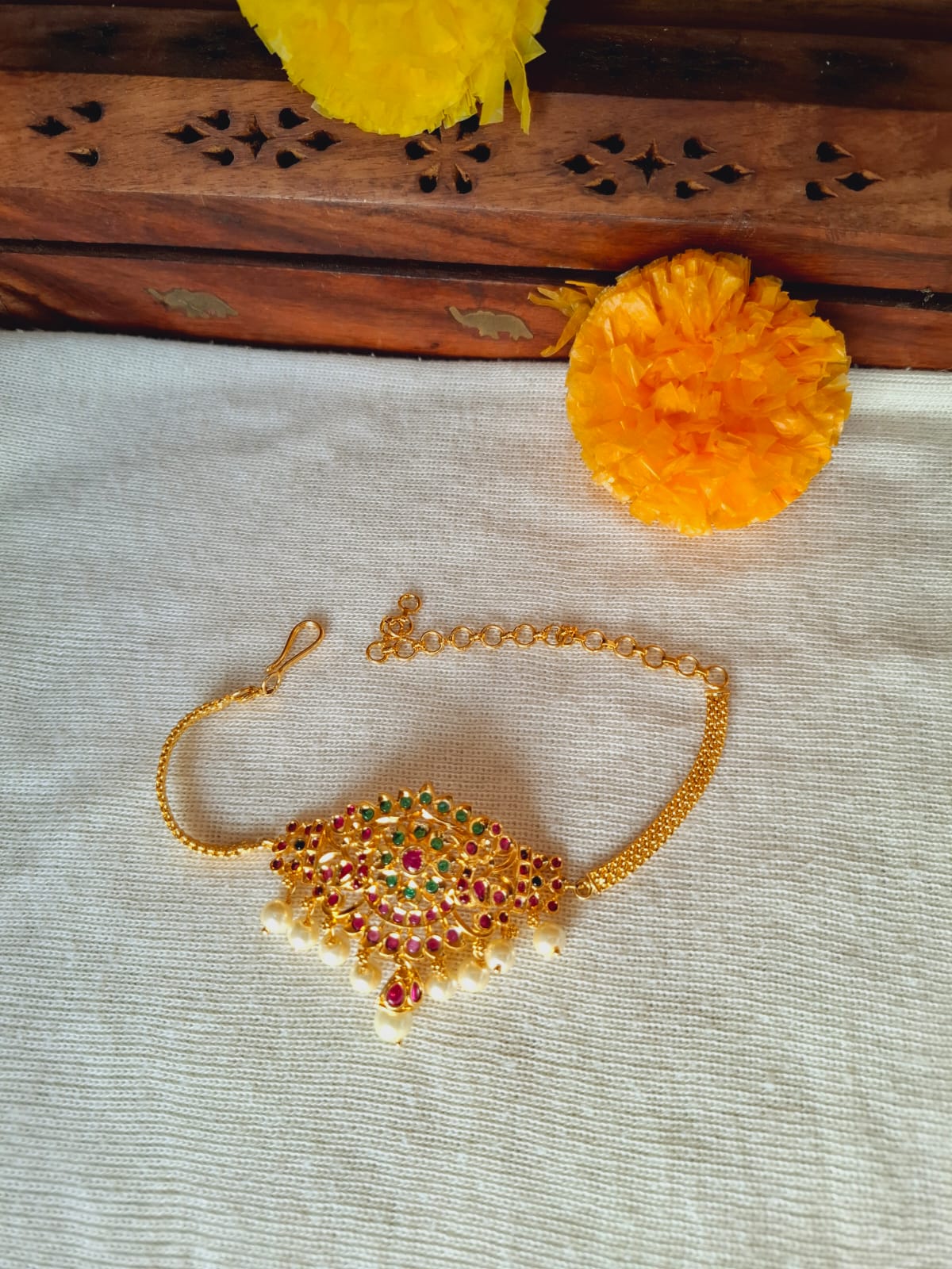 Elegant gold designer bajuband with colorful gemstones on a textile backdrop with yellow flowers