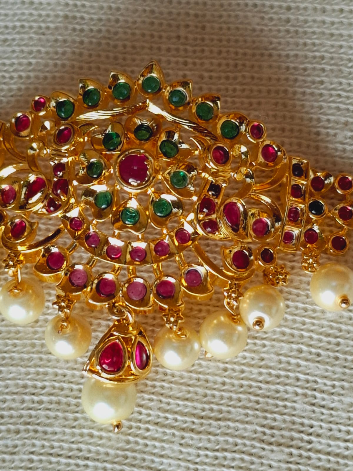 Ornate gold-toned designer bajuband adorned with vibrant red, green, and pearl embellishments, showcasing intricate jewelry craftsmanship.