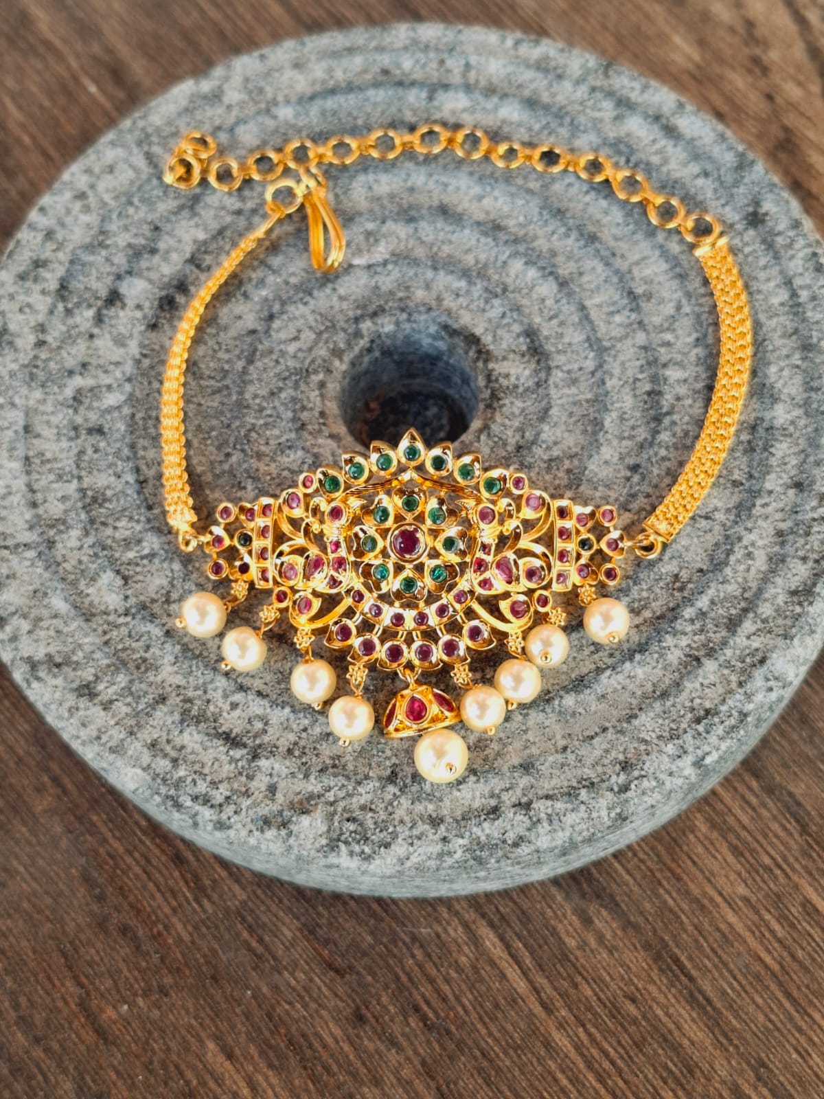 Ornate gold and gemstone bajuband on a grey fabric background