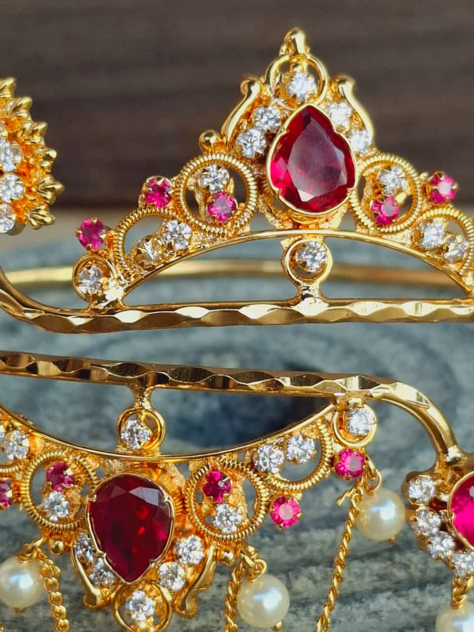 Ornate golden crown with red and white gemstones, displayed against a dark background.