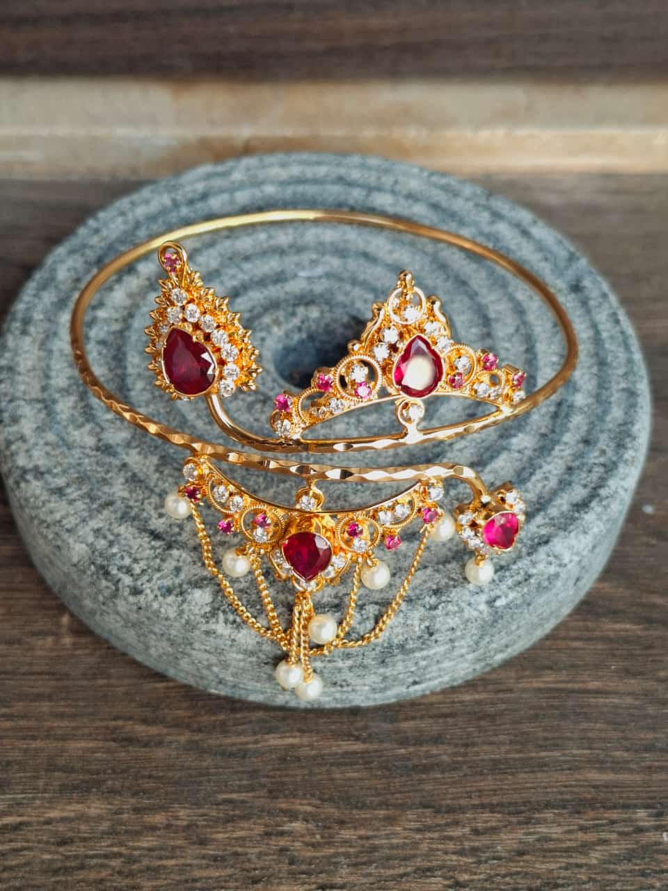 Elegant gold-toned bajuband adorned with vibrant red gems, resting on a cozy grey surface.