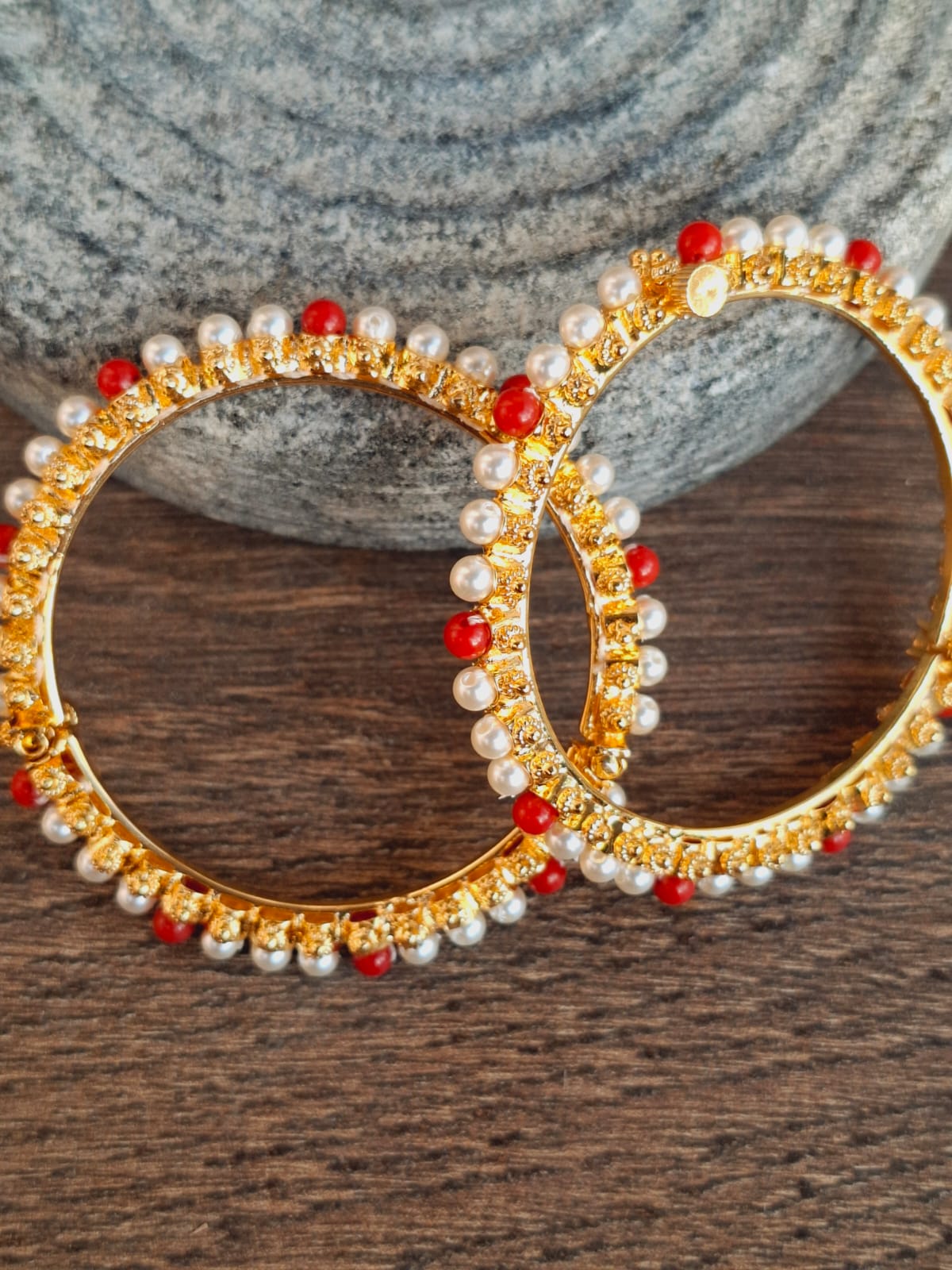 Golden ornate earrings with pearl and red gemstone accents on a wooden surface