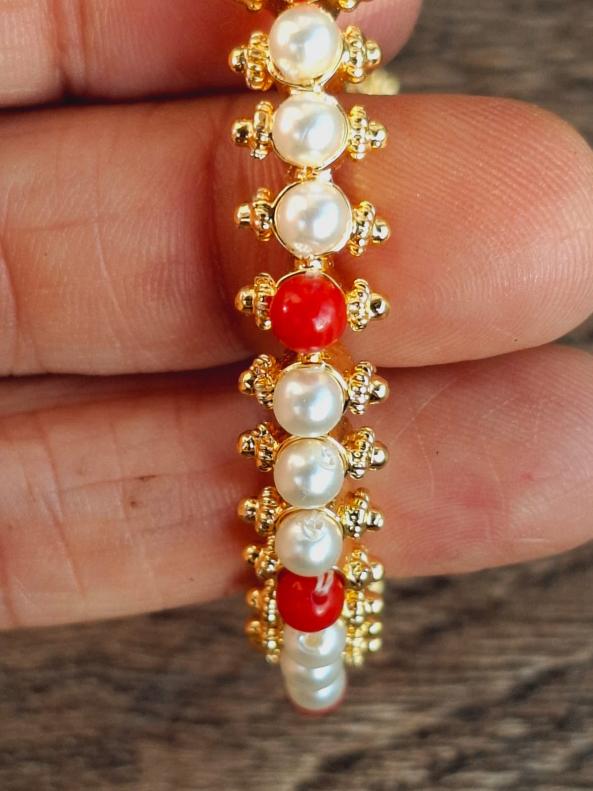 Elegant gold-toned bracelet with alternating pearls and red stones, showcasing intricate craftsmanship and a delicate, luxurious design.