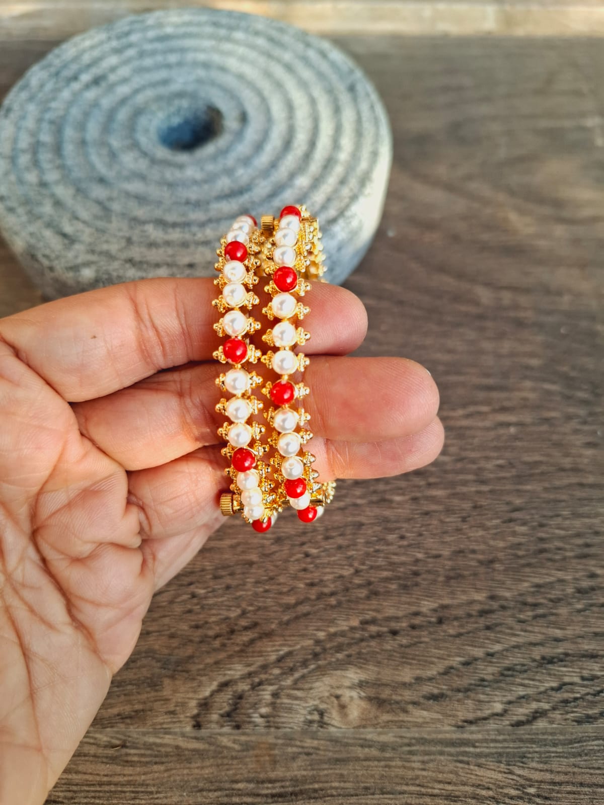 Parinita Tode. Set of 2. Vibrant red and gold beaded bracelets on a wooden surface.