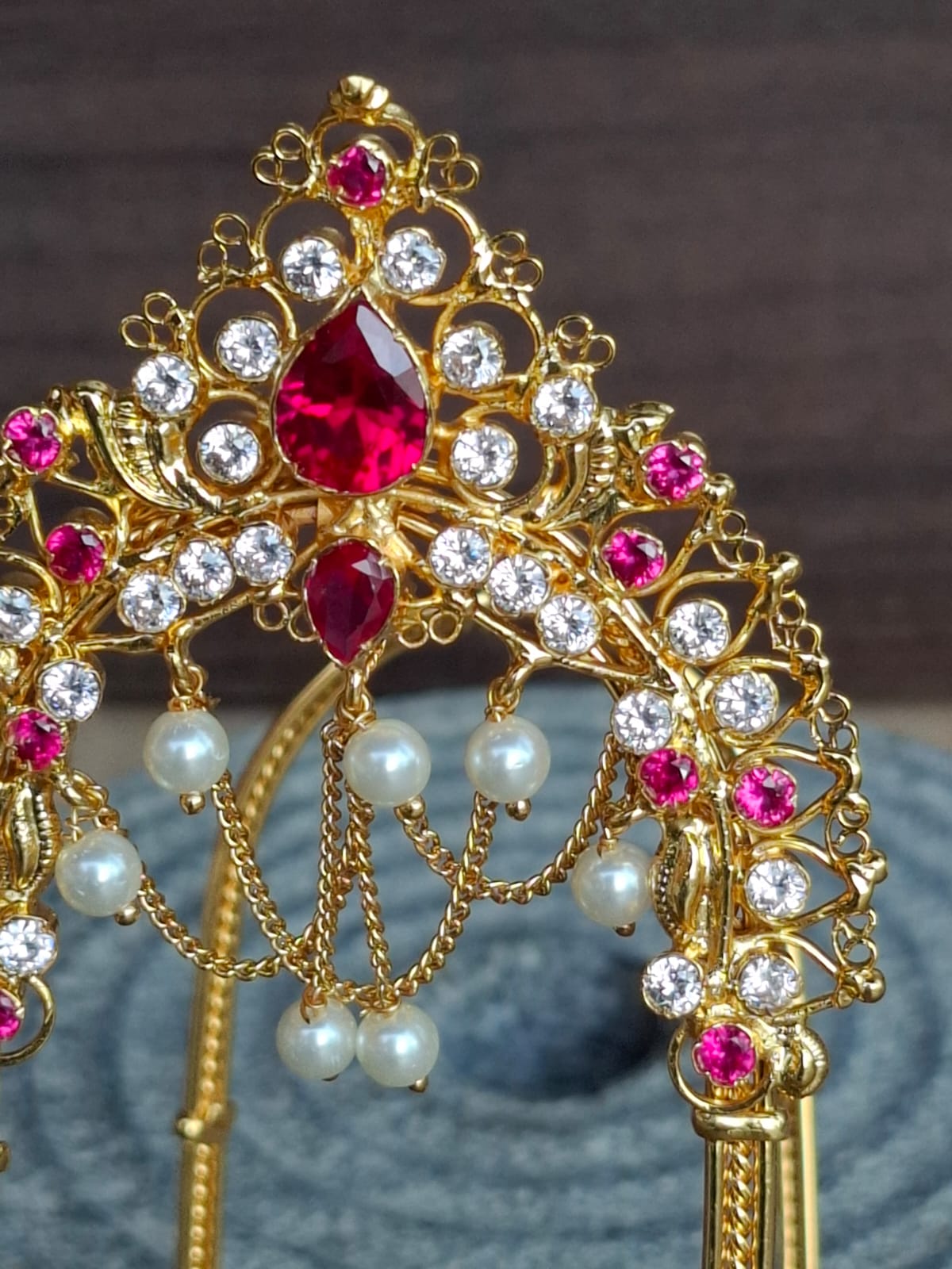 Ornate gold-toned hair accessory with vibrant red and clear gemstones, elegant pearl accents, and intricate floral design for the Mugdha Jewellery Store.