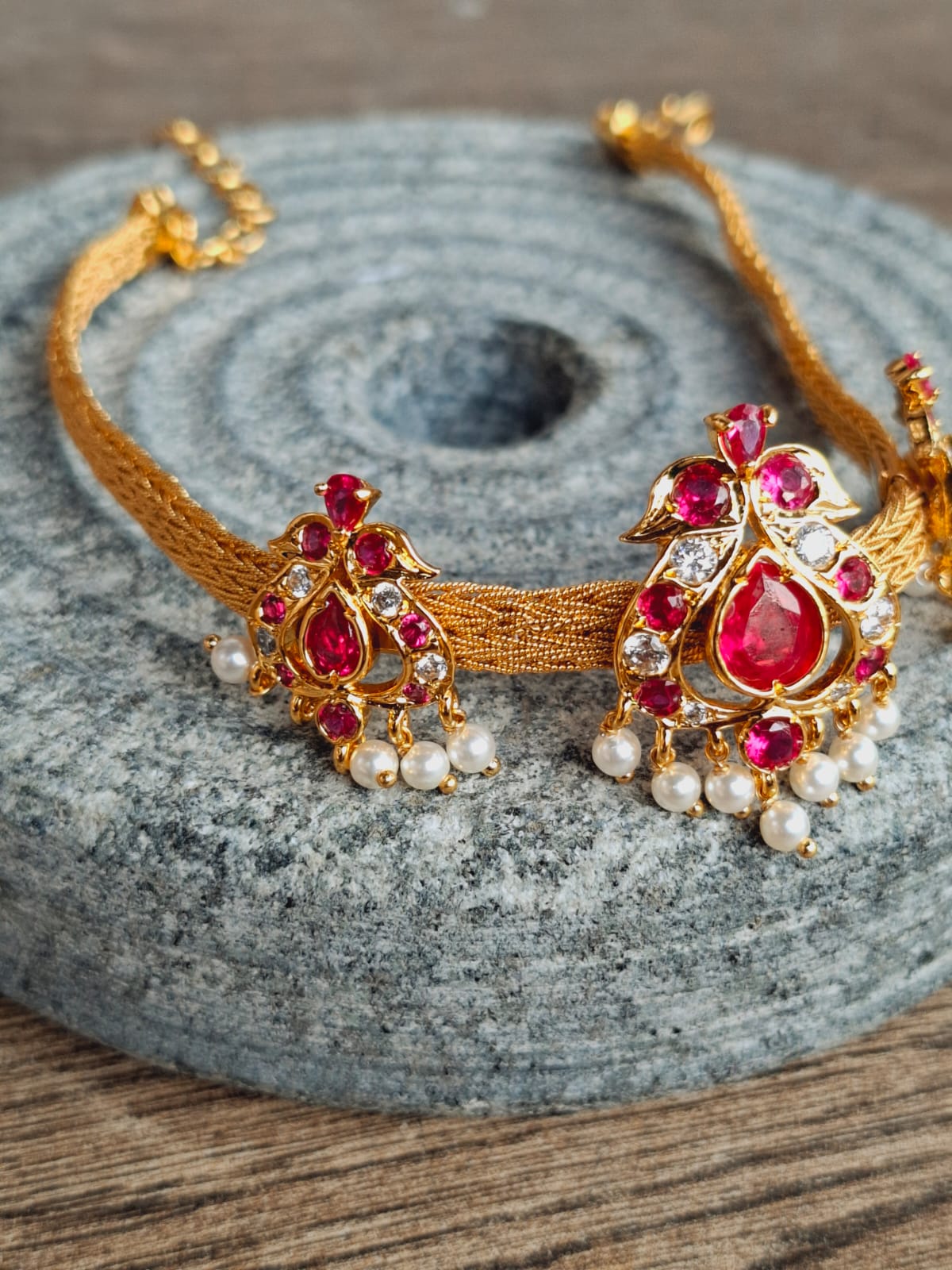 Elegant gold and ruby choker necklace with delicate floral motifs and pearl accents, displayed on a gray stone surface.