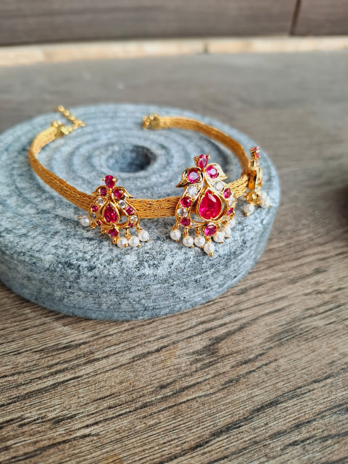 Ornate gold-toned choker and bajuband set with vibrant red gemstones and intricate floral design, elegantly displayed on a gray stone surface.