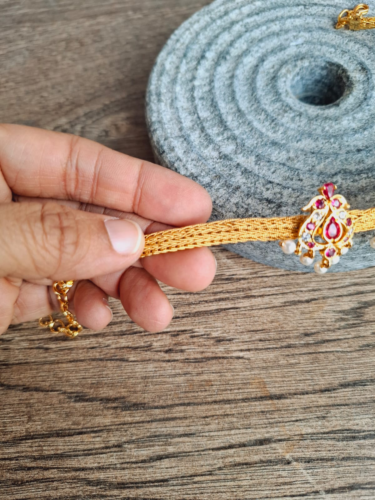 Ornate golden and jewel-encrusted chatai peacock choker and bajuband on a woven grey mat against a wooden background