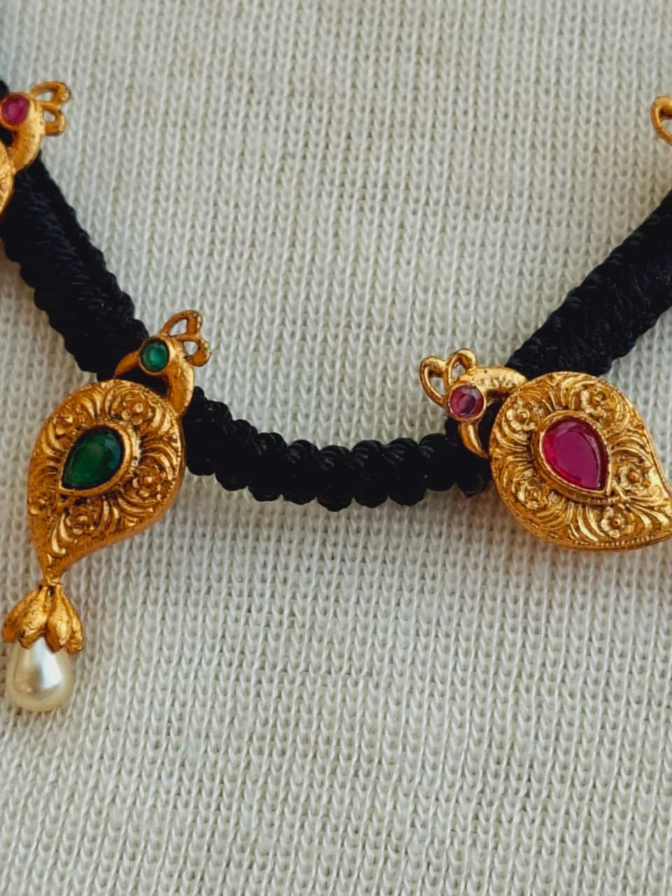 Ornate golden floral pendant mangalsutra with vibrant gemstones on a woven black thread necklace
