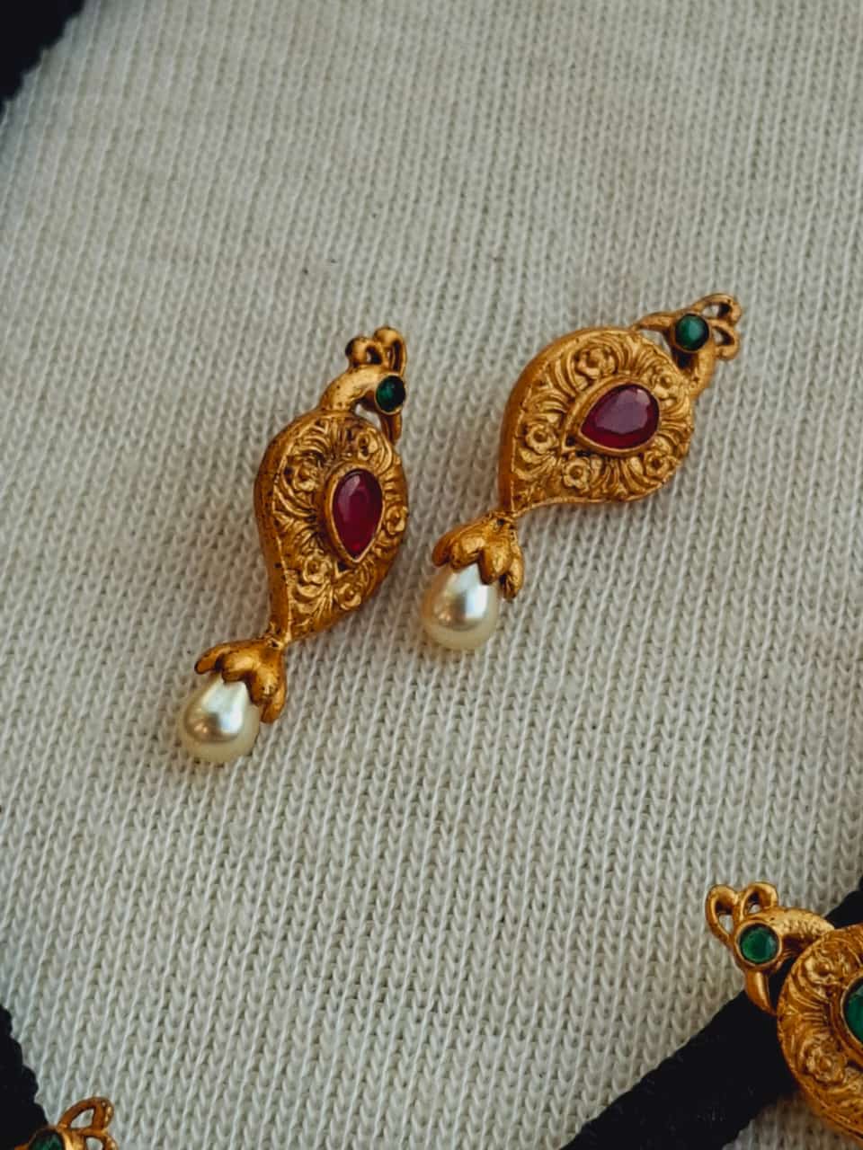Ornate golden Peacock Thread Peshwai Mangalsutra with ruby and pearl adornments placed on a light-colored textile.