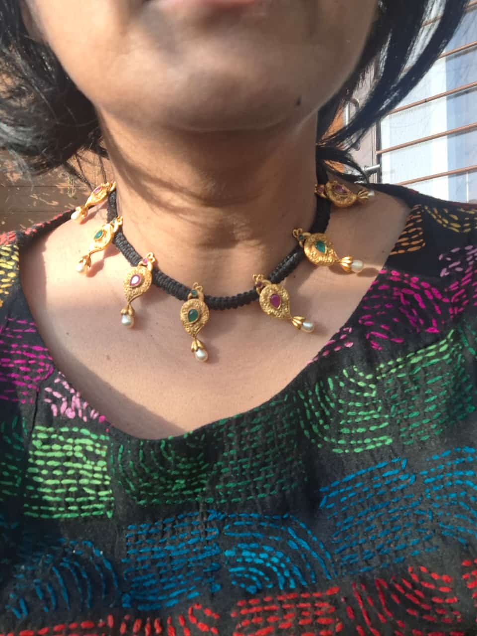 Vibrant and intricate peacock-inspired thread mangalsutra necklace showcased on model's chest against colorful patterned fabric background in Mugdha Jewellery Store.
