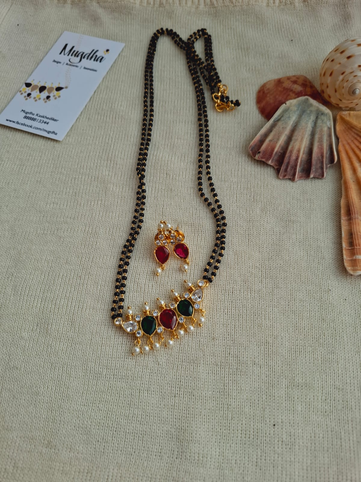 Elegant multicolored Tanmani mangalsutra necklace with gold and gemstone accents, displayed on a neutral background with seashells.