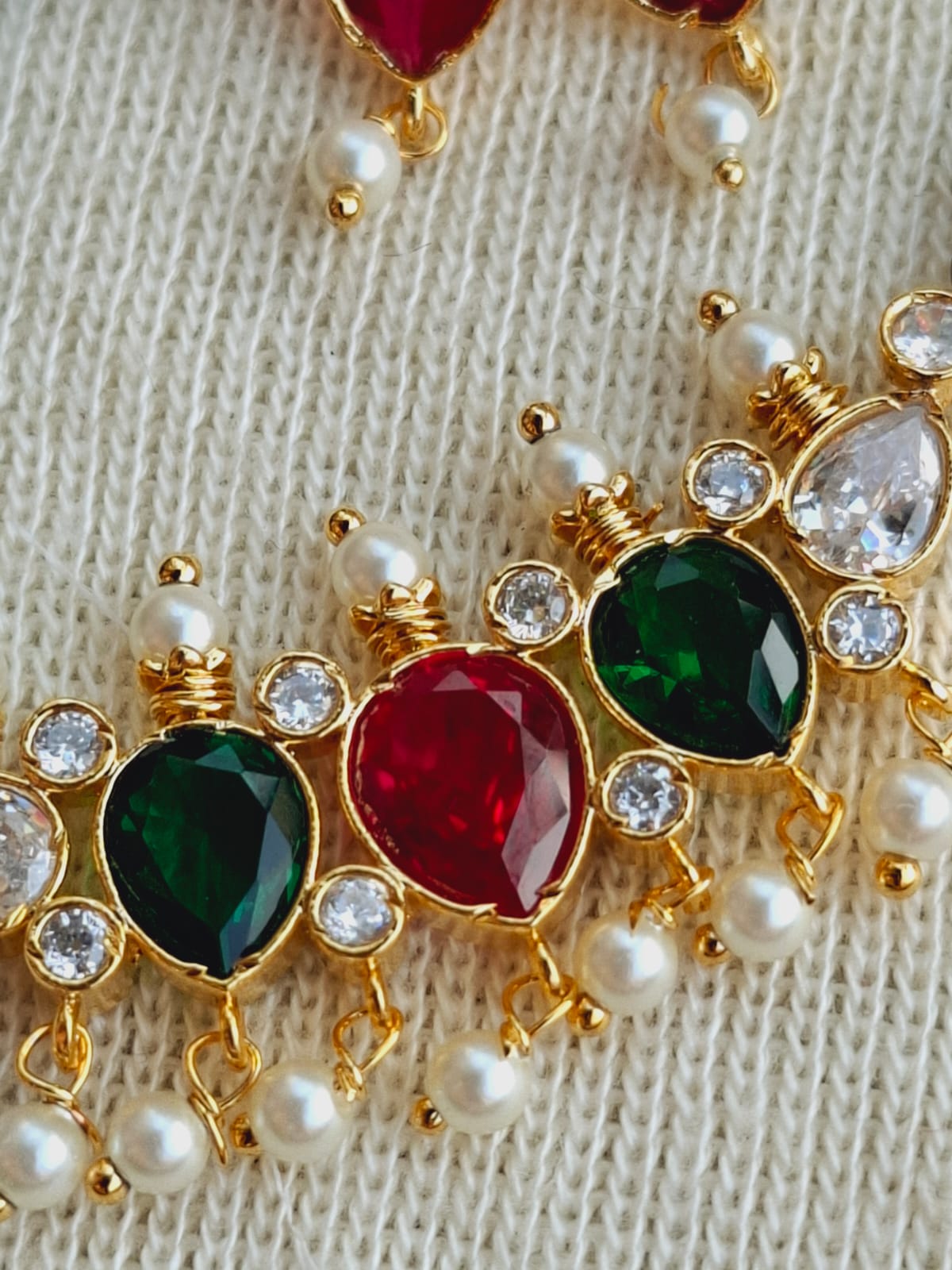 Ornate gold-toned necklace with colorful gemstones and delicate pearls displayed on a textured white surface.