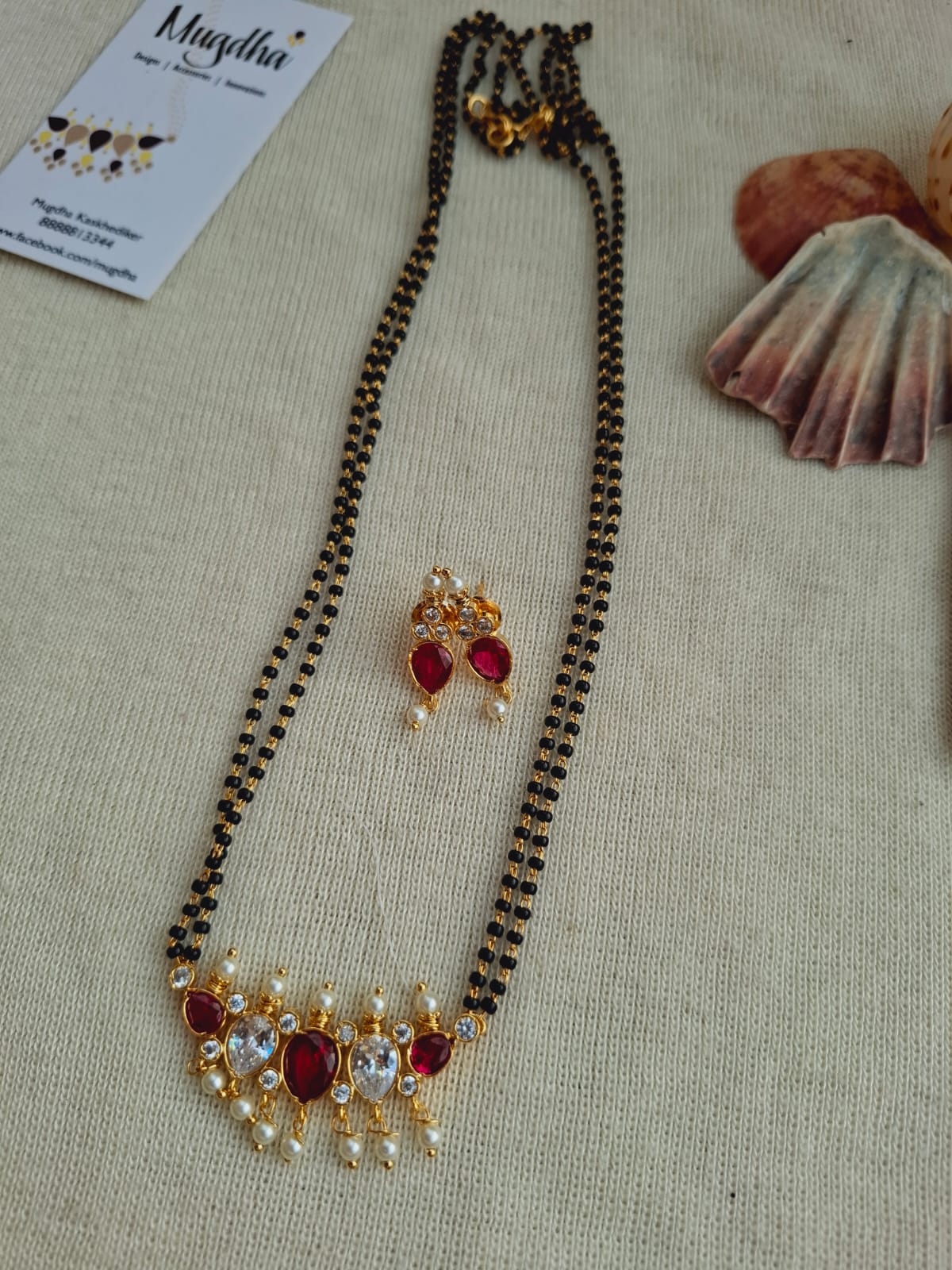 Dark pink and white fancy tanmani mangalsutra with intricate gold accents, displayed on a light-colored fabric background with a store label.