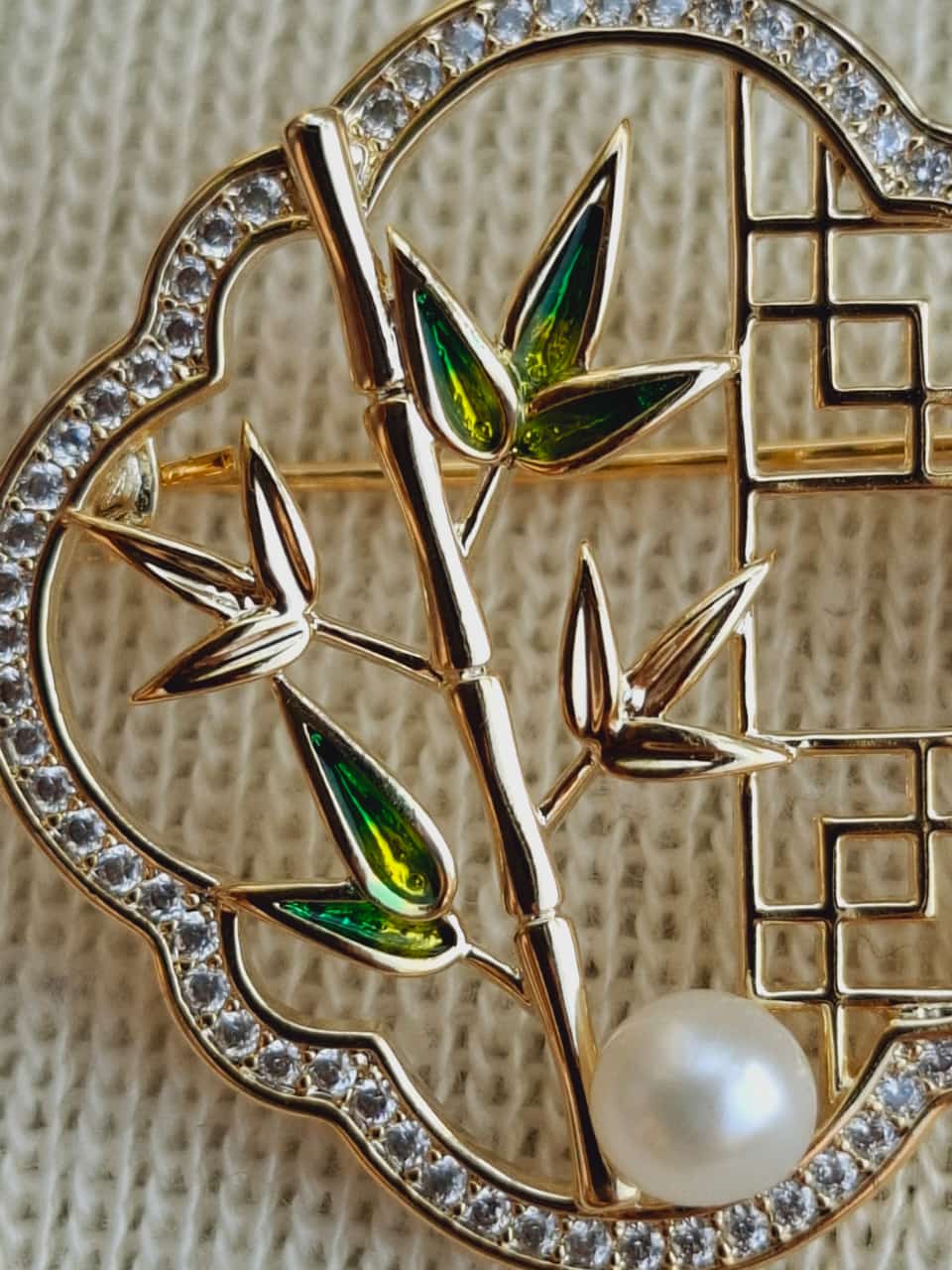Detailed bamboo-inspired brooch with sparkling diamonds, emerald accents, and a lustrous pearl center, set in a stylish geometric design.