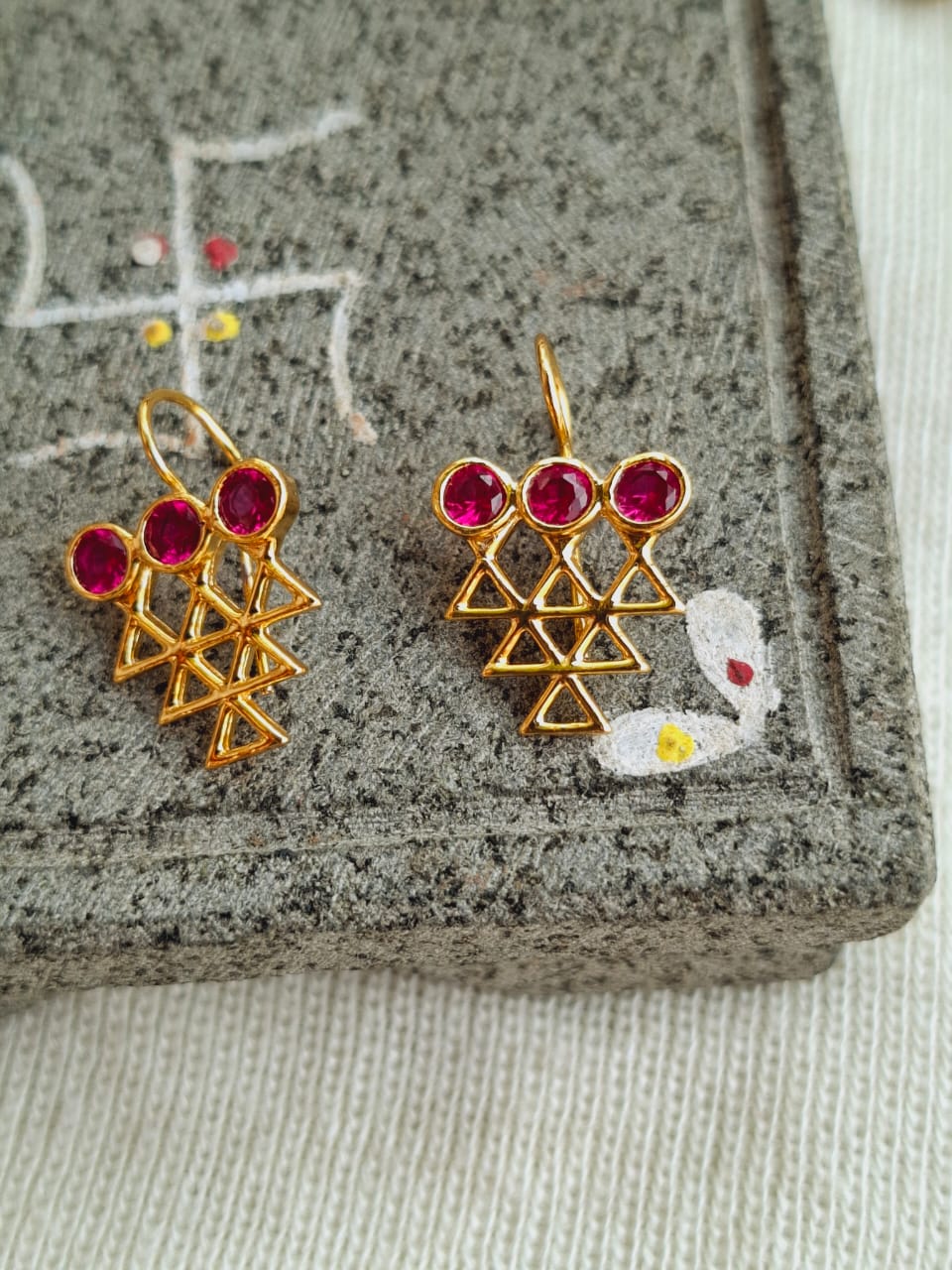 Ornate ruby and gold earrings featuring intricate triangular motifs on a granite surface