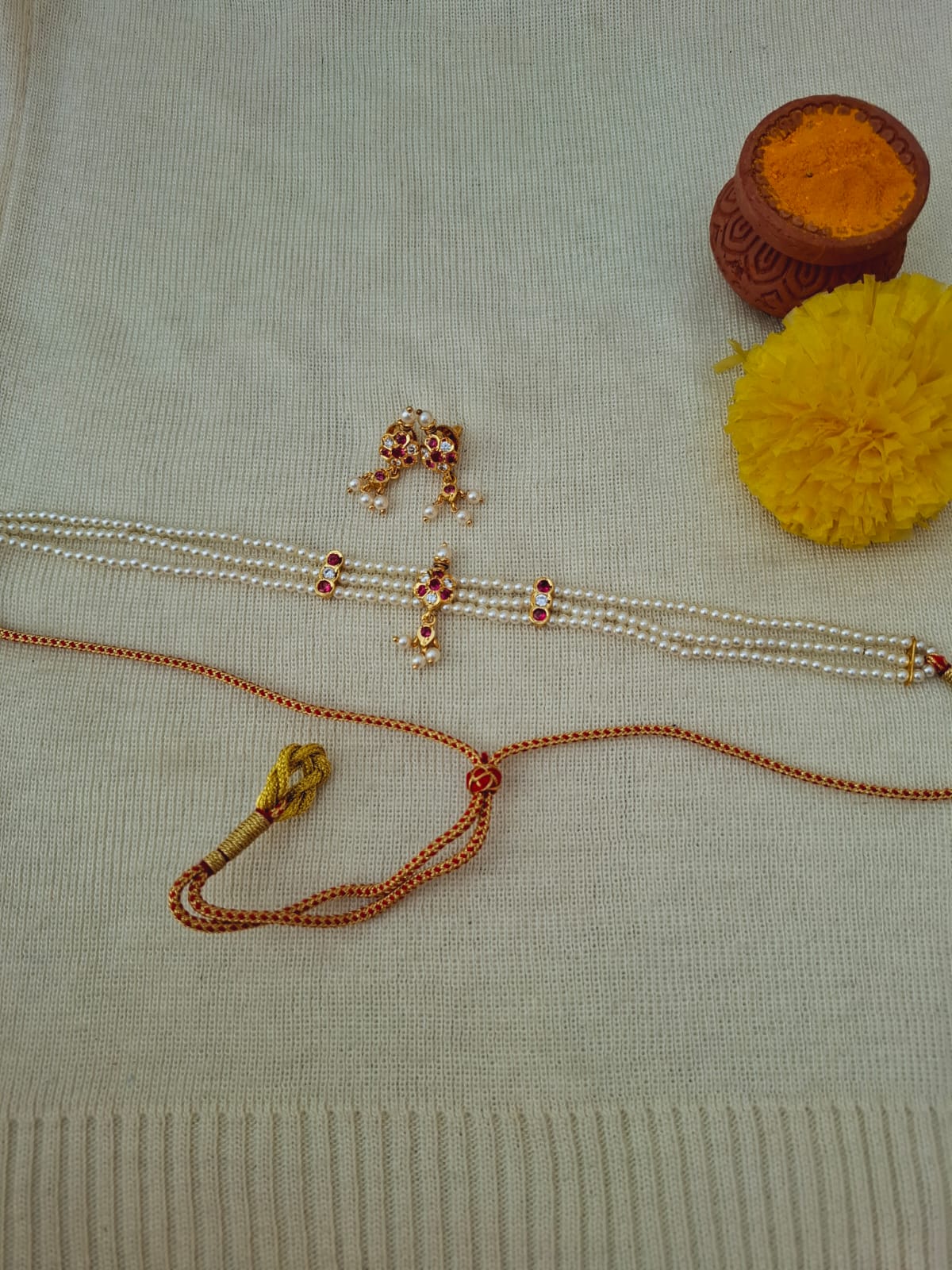 Delicate gold and silver-toned jewelry pieces, including a necklace and small flower-shaped ornament, displayed on a beige textured background with vibrant yellow decorative elements.