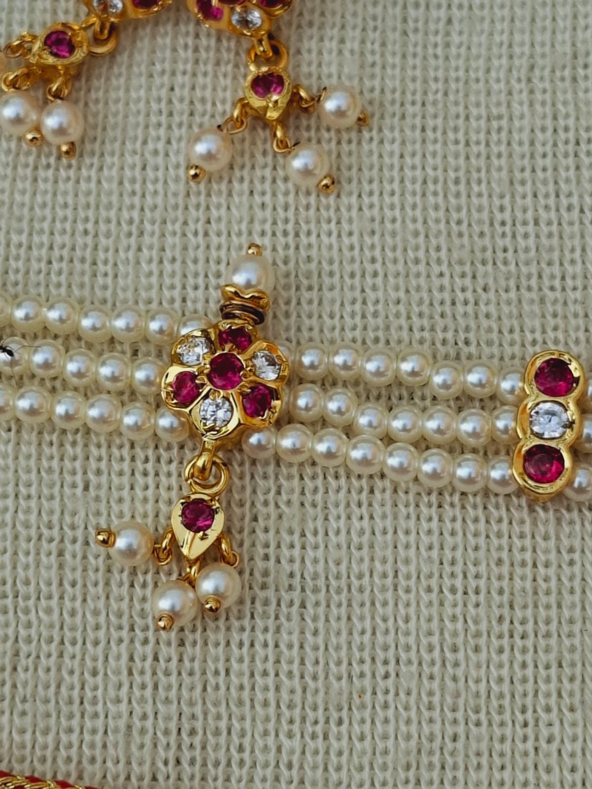 Elegant pearl necklace with floral accents and ruby gemstones, displayed against a light background
