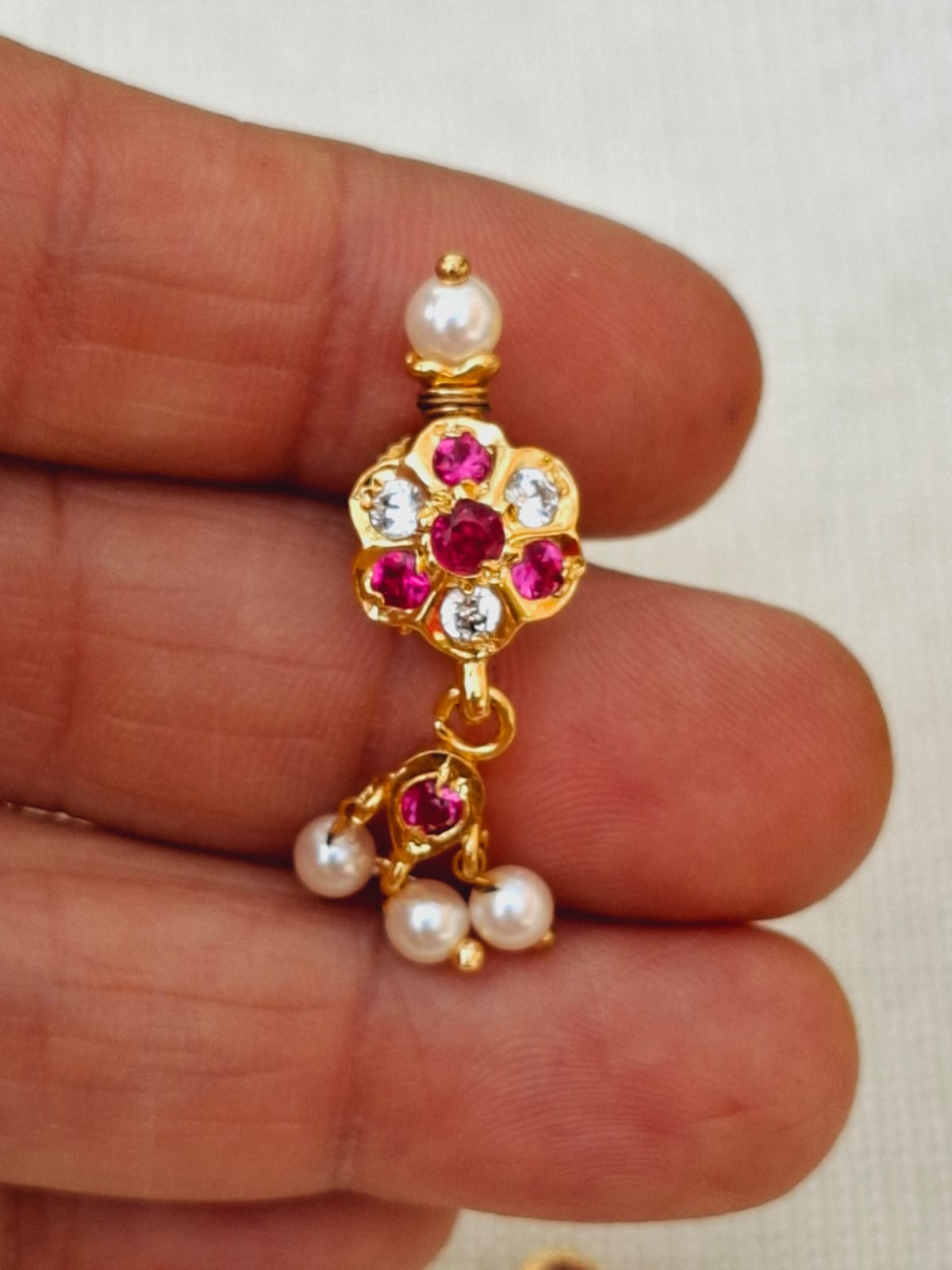 Elegant gold-toned flower-shaped chinchpeti with sparkling rubies and pearls, held in a human hand.
