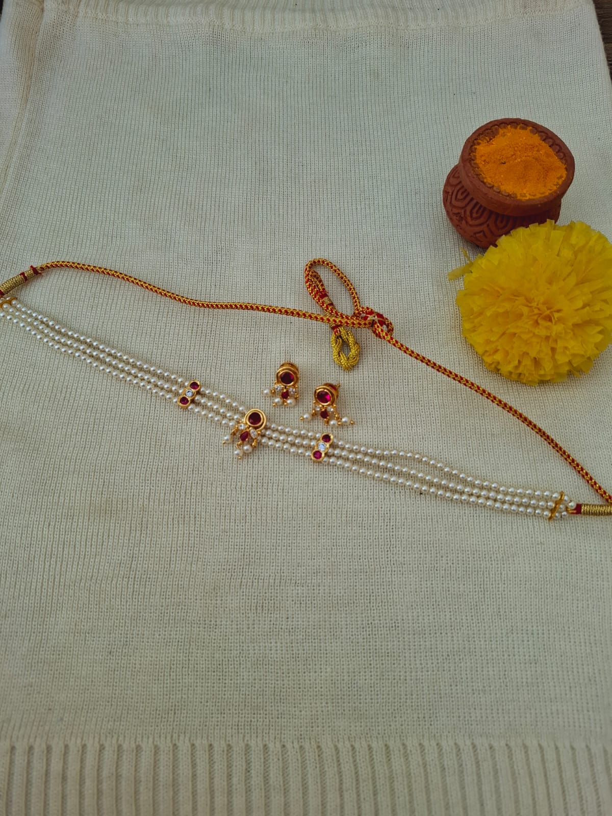 Elegant pearl and ruby necklace with ornamental pompon accents, displayed on a white knitted fabric background.