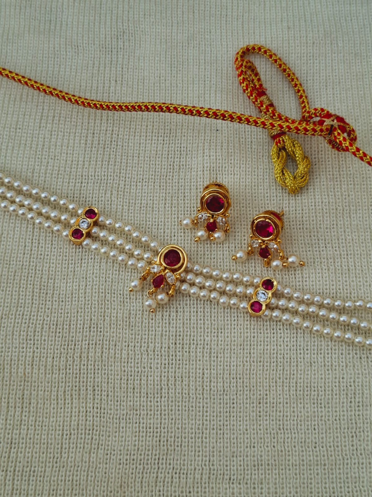 Elegant pearl necklace and earrings with intricate gold and red gemstone accents, displayed on a light gray textured background.