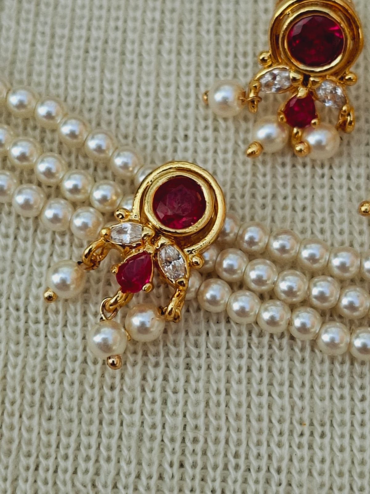 Elegant gold-plated jewel-encrusted Chinchpeti with lustrous pearl beads on ivory fabric background.