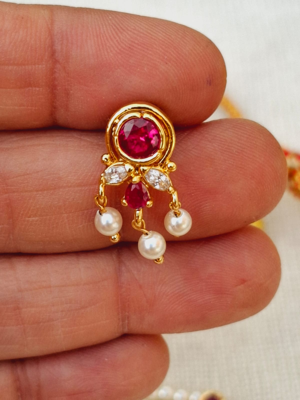 Elegant gold-toned chinchpeti pendant featuring a vibrant red gemstone and sparkling white pearls, showcased in the palm of a hand.