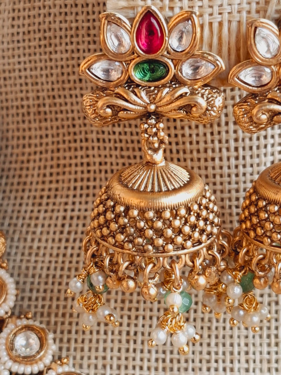 Ornate golden necklace with colorful gemstones and pearls, showcased on a woven rattan background from the Mugdha Jewellery Store.