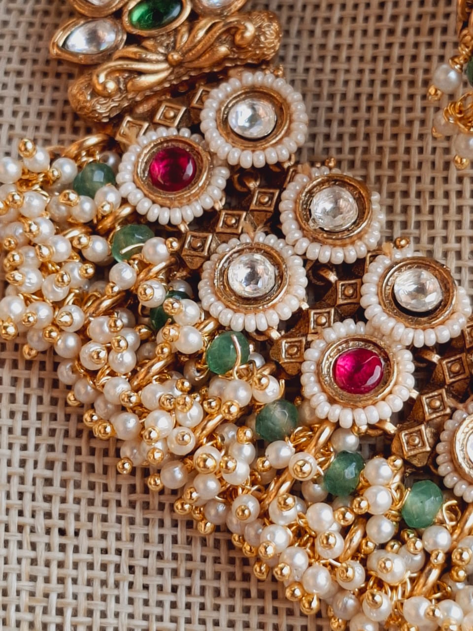 Ornate gold and pearl necklace with intricate floral and geometric patterns, featuring vibrant red and green gemstones in a Mugdha Jewellery Store design.