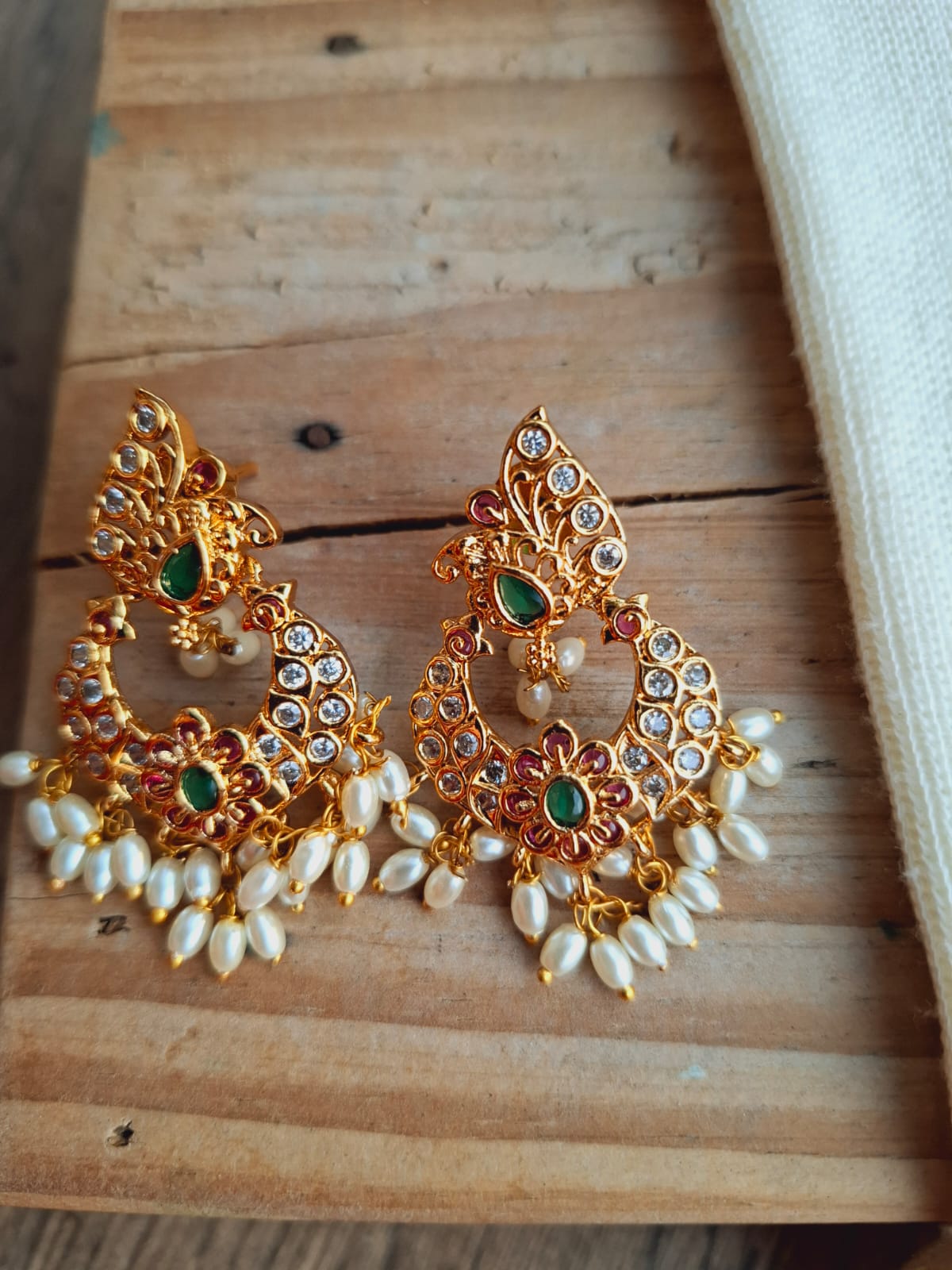 Flower rice pearls earrings with golden floral design and green gemstones displayed on a wooden surface.