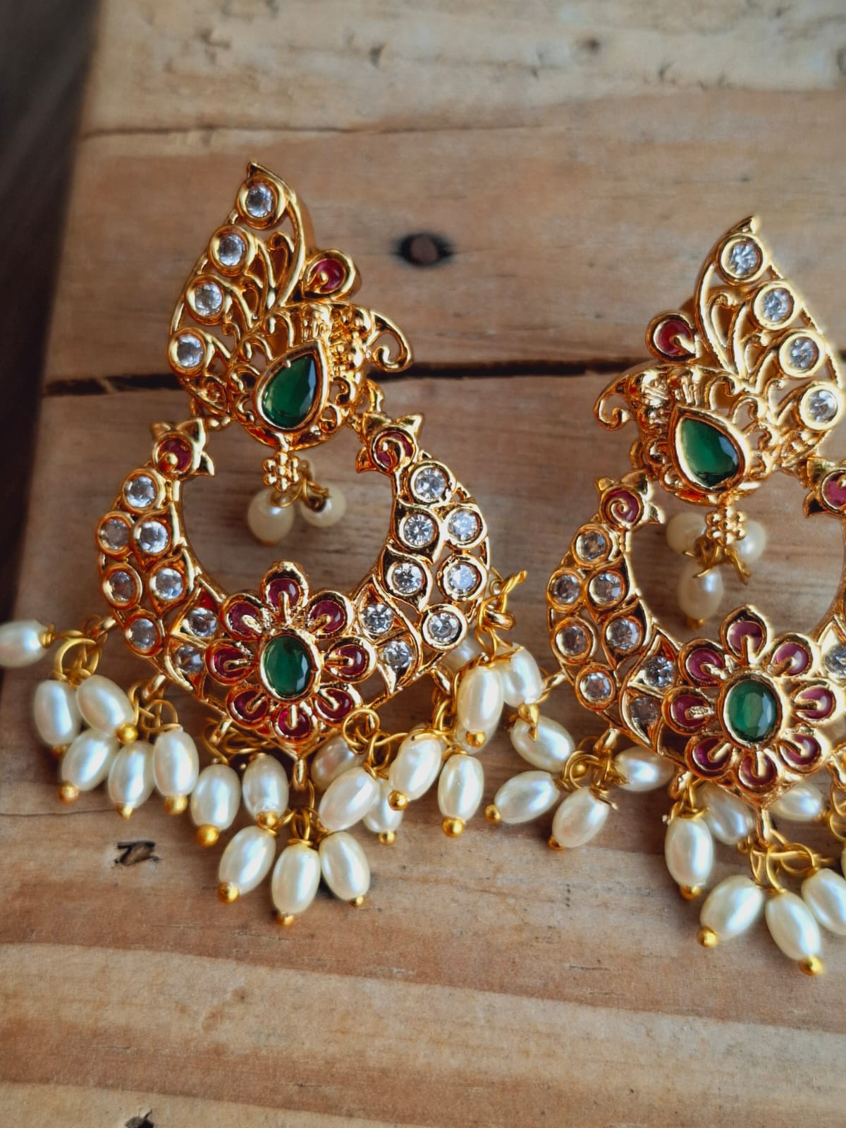 Elegant Floral Jeweled Earrings
Ornate gold-toned earrings with vibrant gemstones, intricate floral designs, and delicate pearls, displayed on a rustic wooden background.