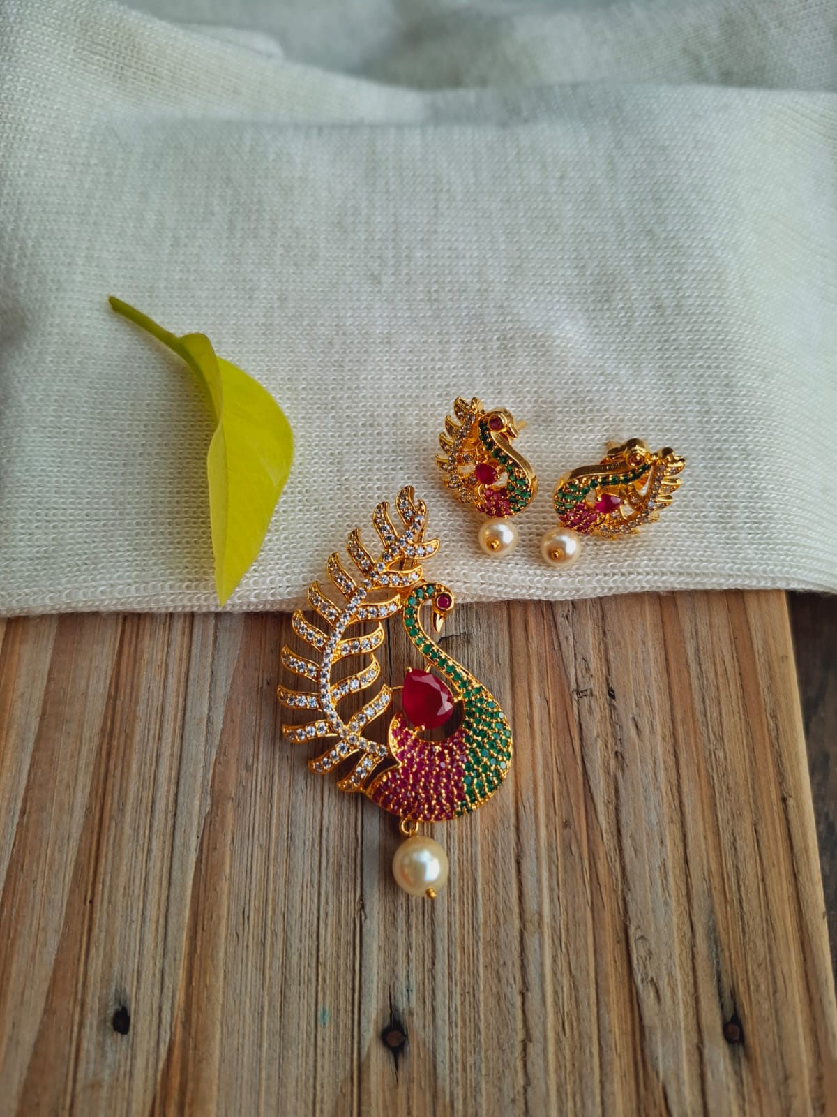 Ornate peacock pendant set with vibrant colored gemstones and sparkling gold-tone accents displayed on a wooden surface.