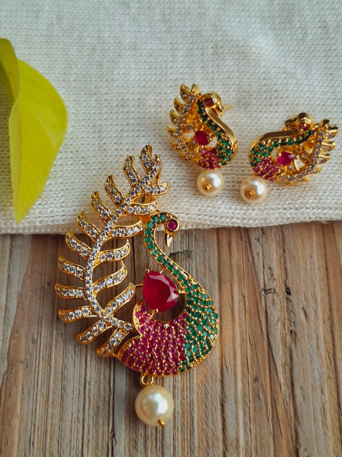 Exquisite peacock-inspired pendant set with vibrant gemstones and pearl accents, showcased on a wooden surface.