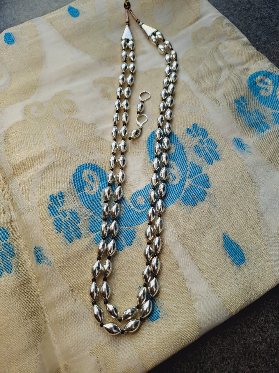 Oxidised long necklace with lyre-shaped dholki beads displayed on a patterned cloth.