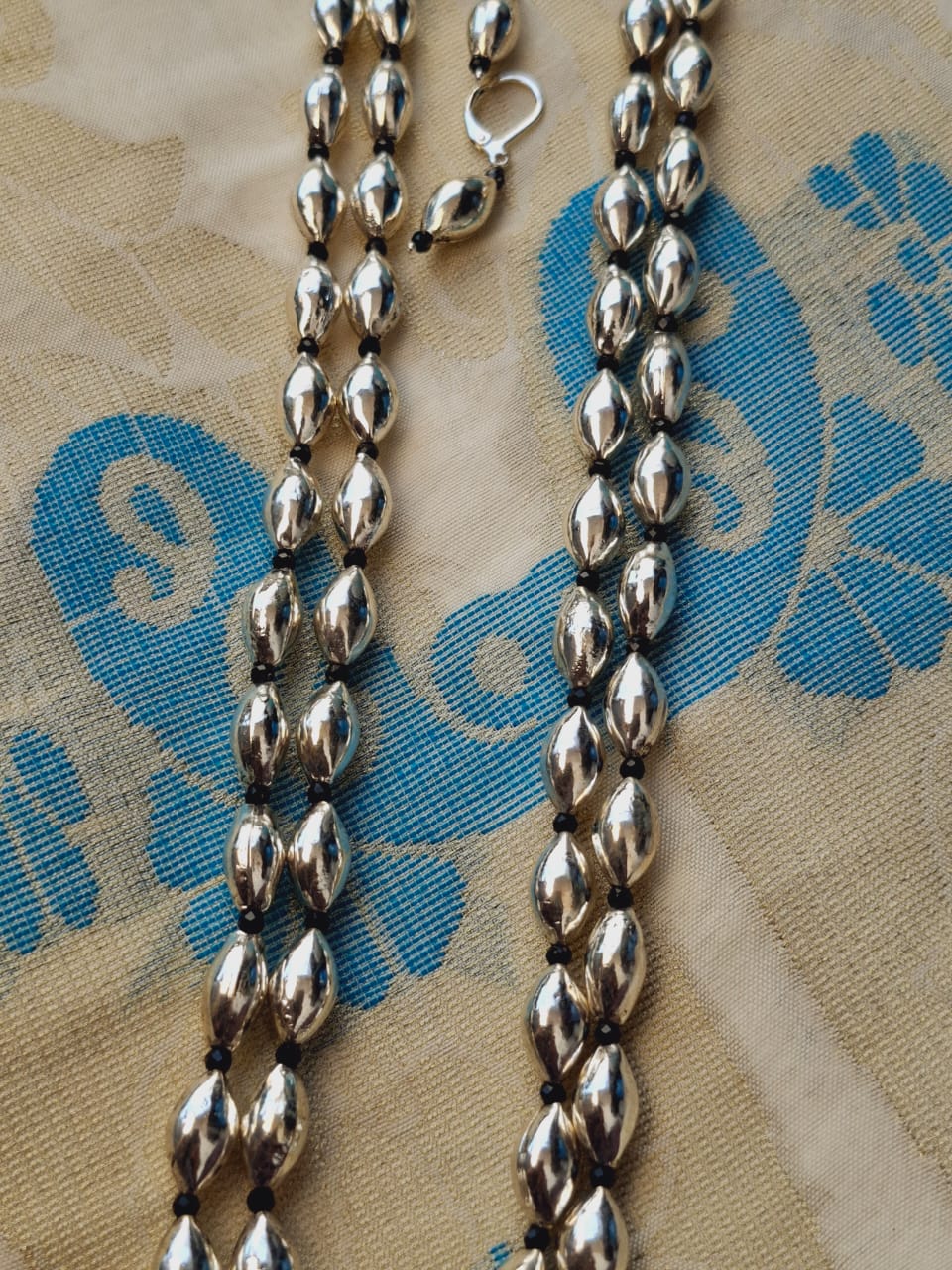 Oxidized metallic long necklace with dholki bead design, displayed on a patterned textile background.