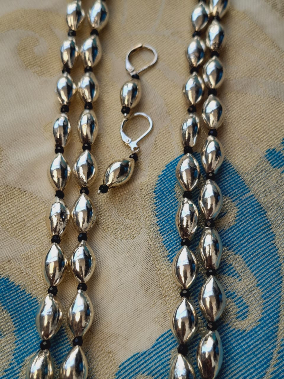 Oxidised long necklace with two lyre-shaped dholki beads displayed on a textured fabric background.