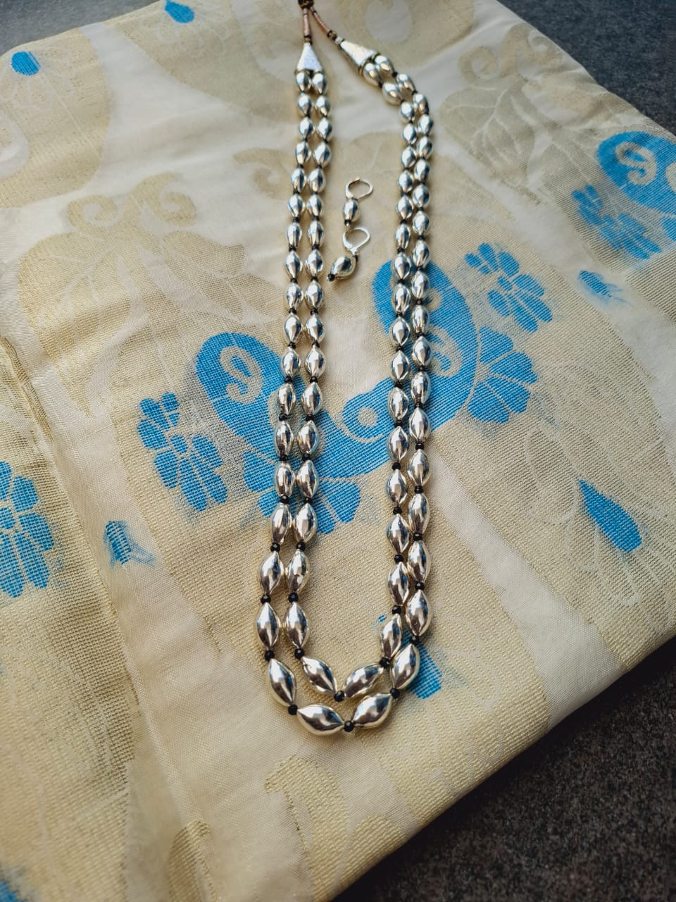 Elegant oxidized metal lyre-shaped bead long necklace from Mugdha Jewellery Store displayed on a patterned textile background.