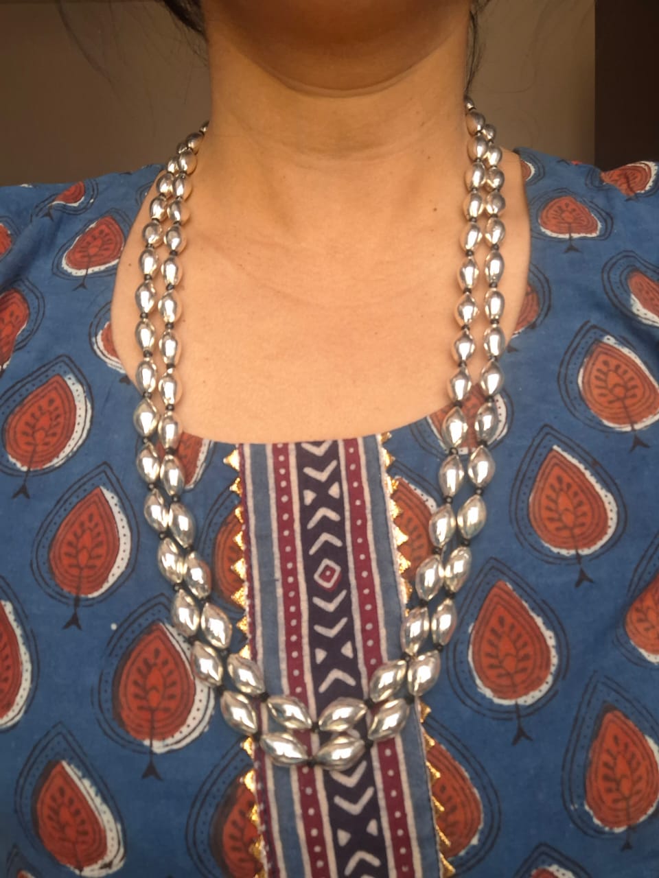 Oxidised metal Lyre Dholki bead long necklace against a patterned blue and orange backdrop